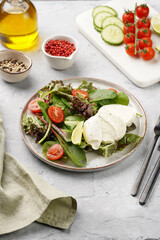 Salad with green leaves, lettuce, spinach, cherry tomatoes, mozzarella, olive oil, chilli pepper, lime juice on grey stone surface