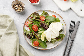 Salad with green leaves, lettuce, spinach, cherry tomatoes, mozzarella, olive oil, chilli pepper, lime juice on grey stone surface