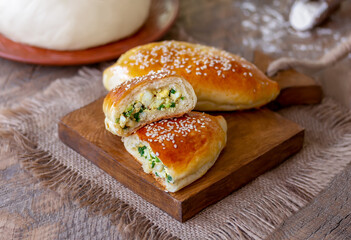 Homemade traditional Russian pies (piroshki) with boiled eggs and spring onion filling with fresh dough and flour on background. Close up, selective focus, wooden table.
