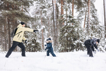 Father and sons having fun snowball fight together in winter forest. Happy children playing in snow outdoors. Christmas holidays, New year family vacation. Brothers in warm clothes walking in cold day