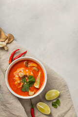 White bowl of fresh Tom Yum soup on a linen napkin with ingredients on a light background
