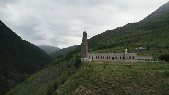 Caucasian battle tower, Ingushetia. Action. Aerial view of an ancient tower and a building on a green hill top surrounded by mountains.