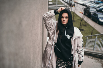 An upset girl stands against a wall on the street. A girl in a black hoodie. Space for text. A teenager in a black hood is offended. 