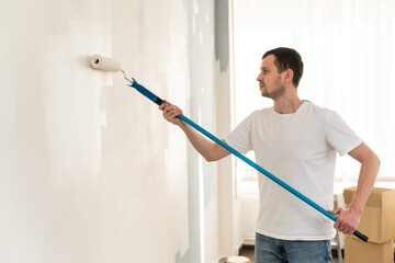 Male painter. Concentrated dark haired man holding dirty paint roller and preparing to repair walls...