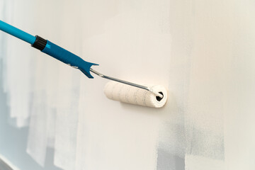 Cropped view of the caucasian man holding paint roller at his hands while brushing walls and...