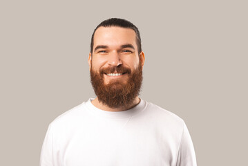 Close up portrait of handsome young bearded hipster man looking at the camera and smiling over grey backdrop.