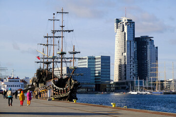 Yacht port in Gdynia, Poland. Silhouette of walking people next to pirate sailing ship.  Skyscrapers on waterfront.