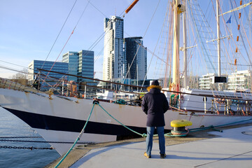 Man standing next to old sailing ship in port of Gdynia, Poland. He looks to ship and skyscraper in...