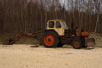 Stara, czerwona koparka -spychacz , stojąca na żwirowym podłożu . An old, red excavator - bulldozer, standing on a gravel ground. 