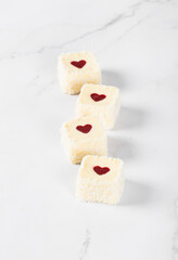 Obraz na płótnie Canvas Festive mousse creamy white chocolate cakes with strawberry jelly heart, in the form of square sweet sushi, sprinkled with coconut chips on a light background. Valentine's Day