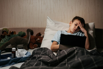 Very sad ill child laying in bed with toys and tablet
