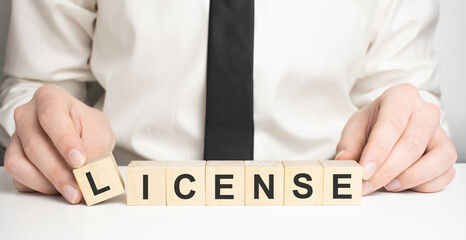 Business person presses his finger on the wooden cubes with the word license. Copyright protection law license property rights.