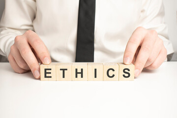 Businessman hand holding wooden cube block with ETHICS business word on table background. Mission,...