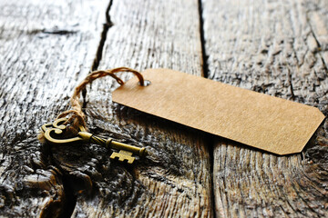 A low angle image of a small brass key with brown paper label on a old wooden desk top. 