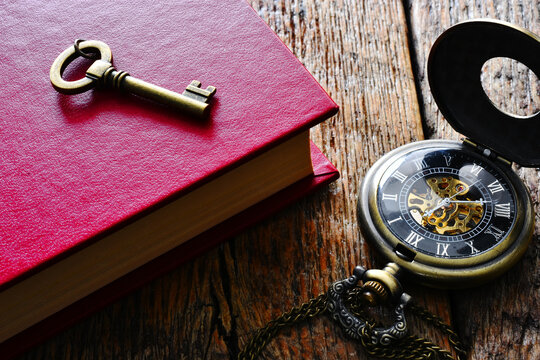 A top view image of a small brass key on a red book with open pocket watch. 