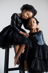 Two african american little sisters keeping eyes closed while posing face to face over white studio background. Concept of family, unity and friendship.
