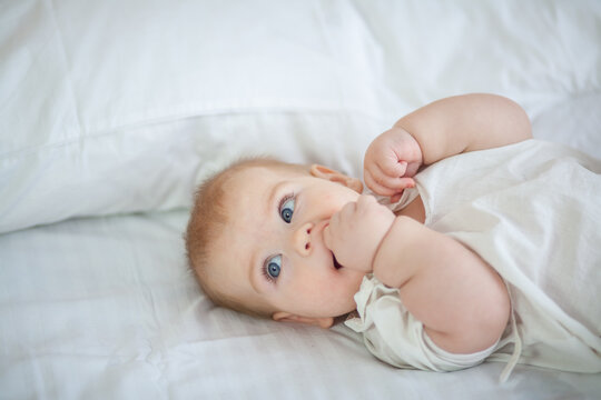 Little newborn baby lies on a white fluffy bedspread.
