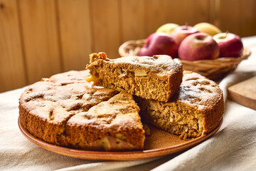 Slice of homemade apple cake Charlotte or american sponge apple pie with walnuts and ripe red apples on the table with linen tablecloth. Healthy seasonal eating.