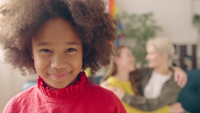 Happy black girl smiling, loving lesbian mothers looking at child and hugging