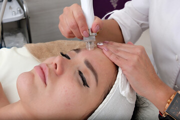 Obraz na płótnie Canvas Facial treatment that allows women to rejuvenate. Dermatologist applies a facial treatment to a young white woman, who is lying in a clinic specializing in skin rejuvenation.