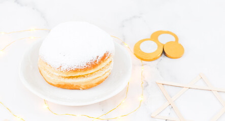 A donut with powdered sugar and cream in a saucer with coins and wooden stars of David.