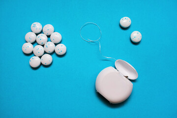 Dental floss for cleaning teeth and round chewing gums on a blue background. The concept of oral...