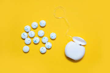 Dental floss and mint-flavored round chewing gums on a yellow background. The concept of oral care...