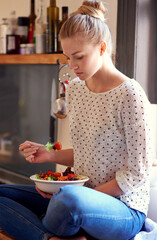 Feeling good starts with eating right. Shot of a young woman eating a healthy salad in her kitchen.