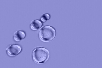 Cosmetic hydrating product or ingredient concept. Blue drops of transparent liquid on a very peri background. Drops gel or oil close up. Abstract backdrop.