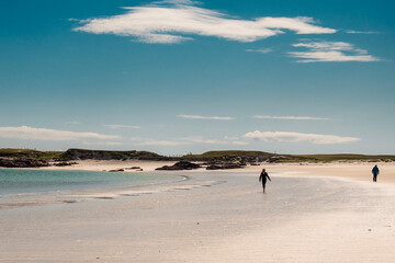 Beautiful seascape scene. Silhouette of people. Light yellow sandy beach and blue ocean surface. Gurteen bay, county Galway, Ireland. Dramatic cloudy sky. Irish landscape. Popular travel destination.