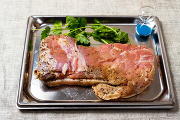 Raw pork belly on a metal tray with fresh coriander and small sand clock for cooking timing. Fresh meat product.
