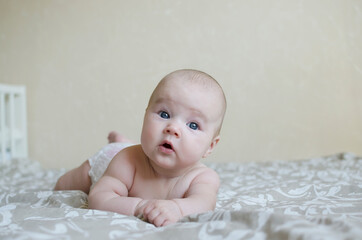 Cute little baby girl on the bed close-up lies on her stomach and smiles .Childhood, mothercare concept