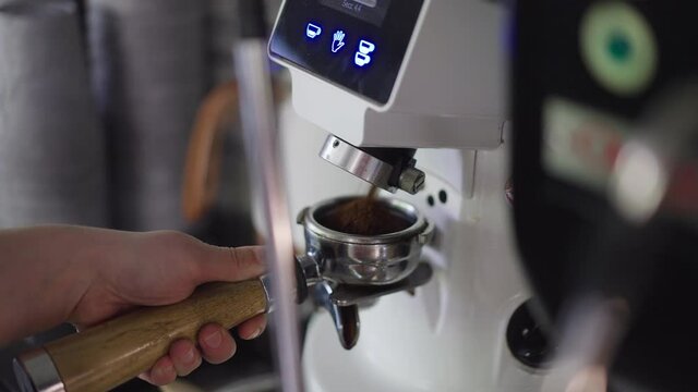 Close-up coffee maker grinding coffee into filter holder in slow motion. Process of delicious freshly brewed coffee preparation in restaurant cafe indoors
