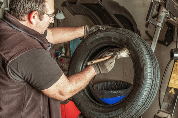 Man applying lubricant to a tyre using a brush in a garage