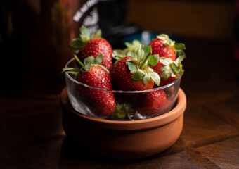 Juicy organic strawberries in a glass - ceramic bowl on wooden table with a soft light.