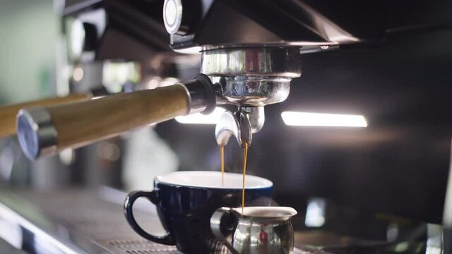 Close-up coffee pouring in cup in slow motion from espresso machine in coffee house. Unrecognizable female barista preparing tasty delicious freshly brewed drink indoors in slow motion