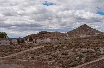 Tonopah, Nevada, US - May 19, 2011: Newly constructed houses in neighborhood set on dry brown desert floor with hills in back under thick blue cloudscape.