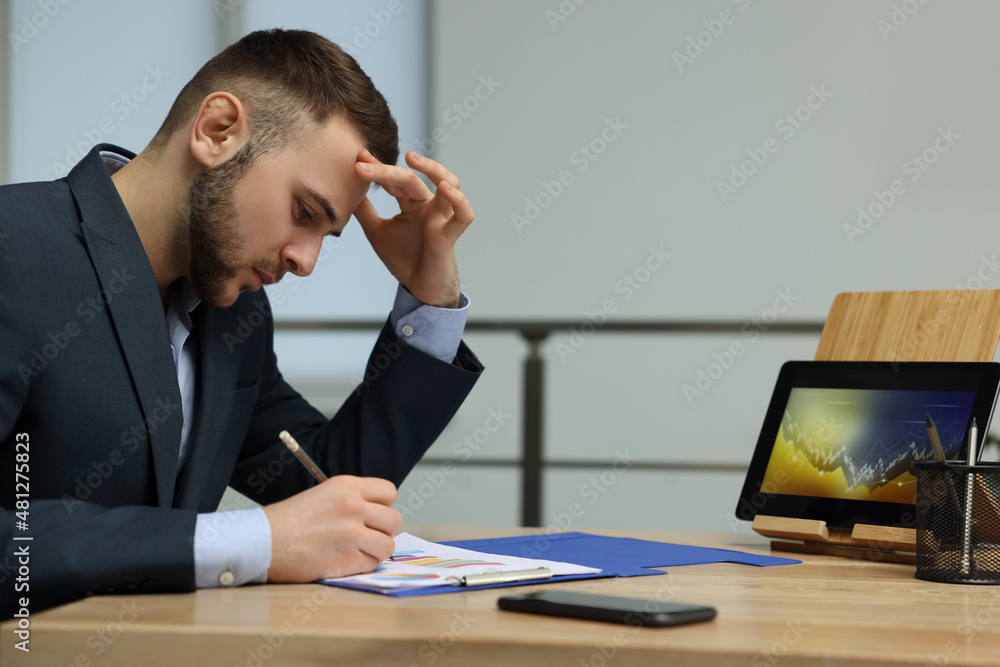 Poster forex trader working with tablet and documents at table in office