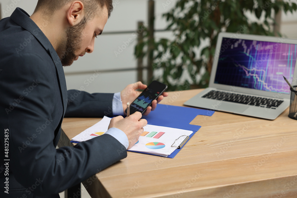 Poster forex trader working with smartphone and charts at table in office