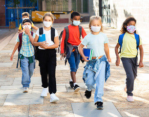 Kids in face masks walking after lessons keeping social distance at warm autumn day, the new normal