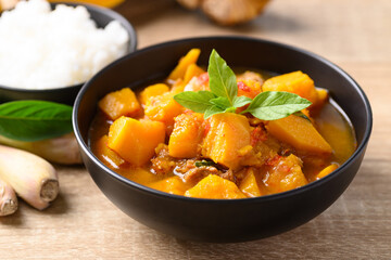 Thai spicy pumpkin curry soup with pork  and cooked rice on wooden table