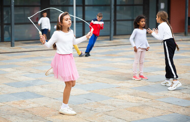 Cute tween girl in pink skirt jumping rope in school yard during recess in warm fall day.