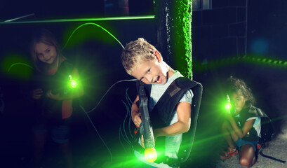 Emotional teen boy with laser pistol playing laser tag with friends on dark labyrinth. High quality...