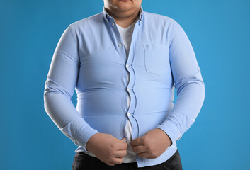 Overweight man trying to button up tight shirt on light blue background, closeup