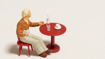 テーブルの上の飲み物を取ろうとする老婆の人形