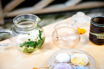 Green tea leaves in glass teapot with colorful mochi rice cake Japanese dessert daifuku on wooden table still life closeup