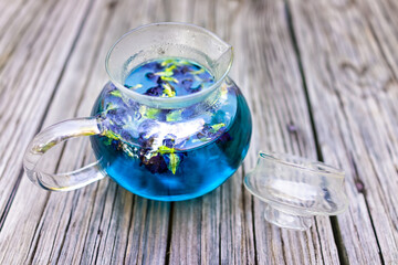 Obraz na płótnie Canvas Butterfly pea blue flower Clitoria ternatea colorful color tea in glass teapot on wooden table background with vibrant vivid deep dye pigment color