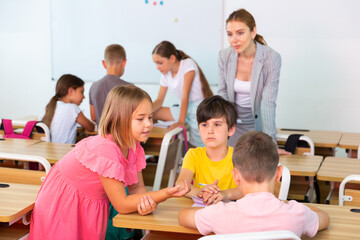 Obraz premium Kids performing group tasks during lesson. Teacher standing and watching them exercising.
