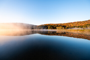 Spruce Knob lake blue water in West Virginia mountains fall autumn season and fog mist sunrise morning glowing yellow orange sunlight in Monongahela National Forest trees foliage