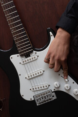 black electric guitar and a musician's hand on the guitar, the guitarist has rings on his fingers.